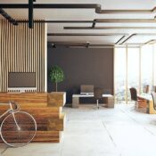 Modern office with large windows, wooden accents, and minimalist desks. A bicycle is parked inside, and a potted plant sits near a black wall. Natural light fills the spacious, open-layout workspace.