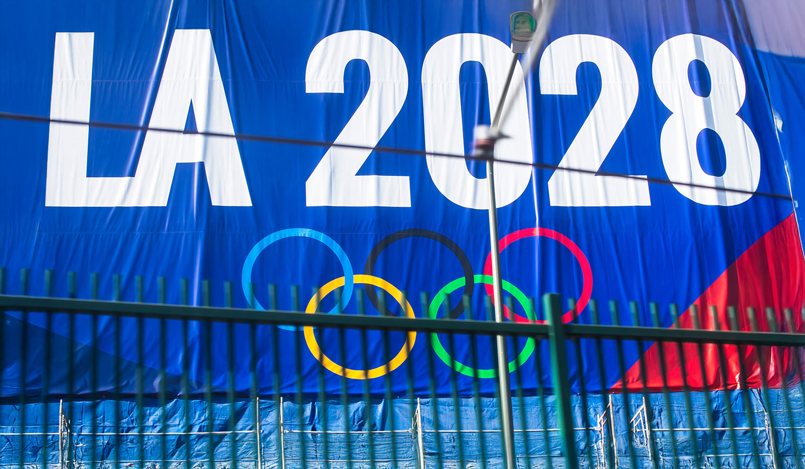 A promotional banner for the LA 2028 Olympics featuring the Olympic rings, displayed on a blue background